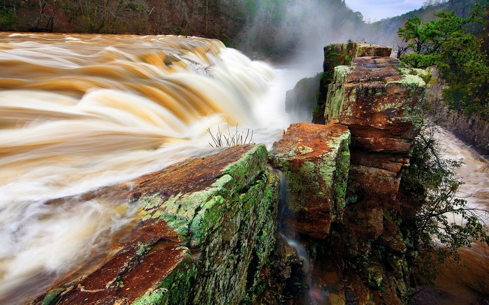Muddy waterfall cascading over mossy rocks