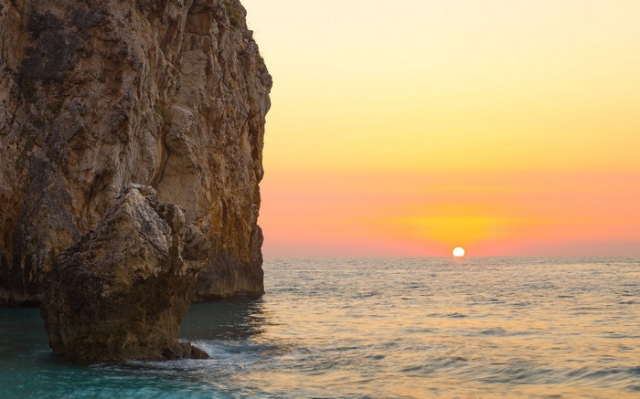 Sunset over the ocean with a rocky cliff
