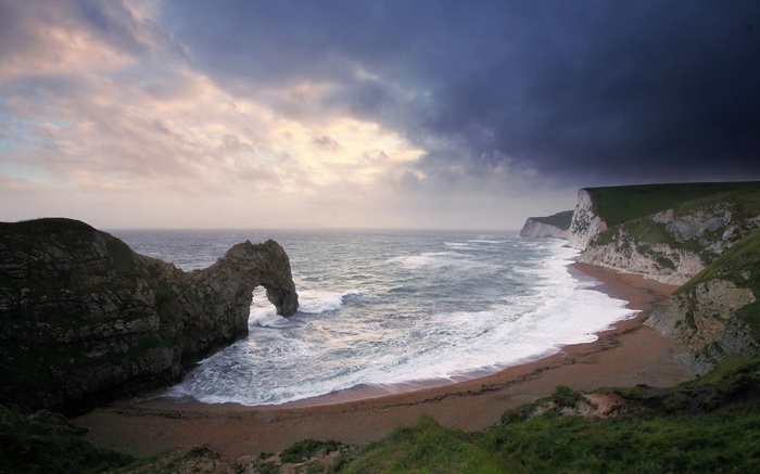 Durdle Door rock arch on a beach with stormy clouds