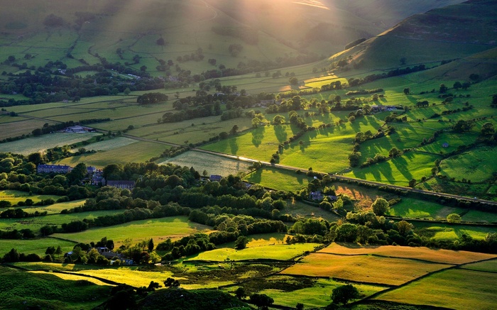 Sunlight illuminates a rolling green valley with scattered trees and buildings.