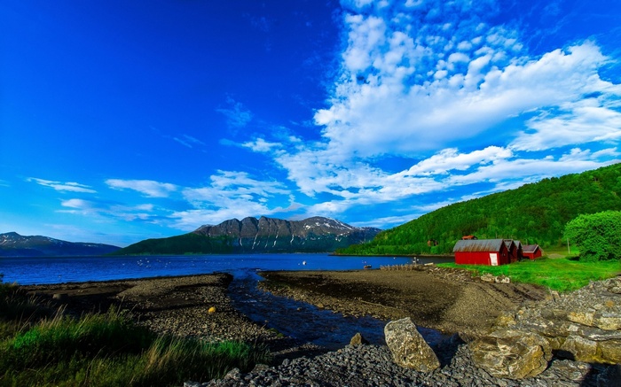 Red cabins by a lake with mountains and blue sky