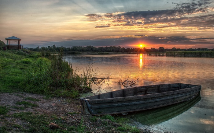 Wooden boat on a lake at sunset with a gazebo