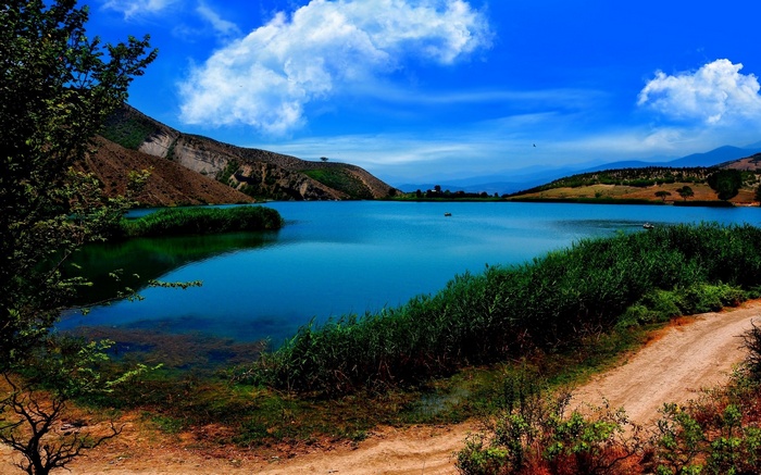 A scenic lake with mountains and reeds under a blue sky