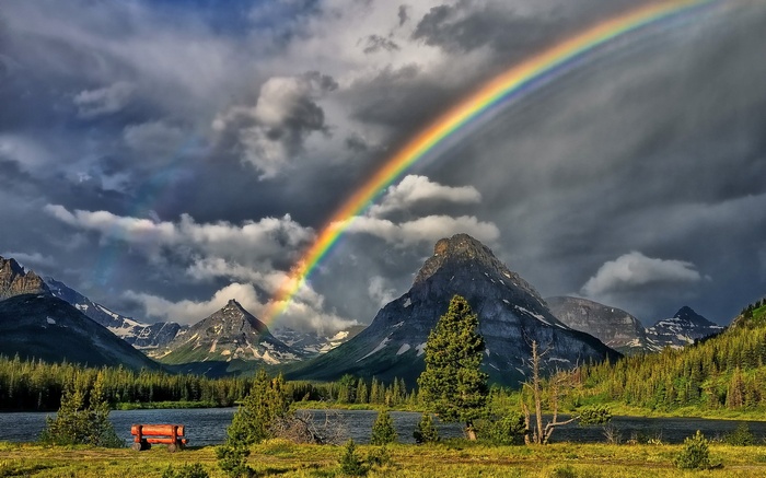 Rainbow over mountains and lake with a bench