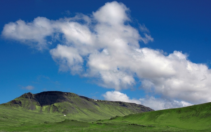 Green rolling hills and a mountain under a blue sky with clouds