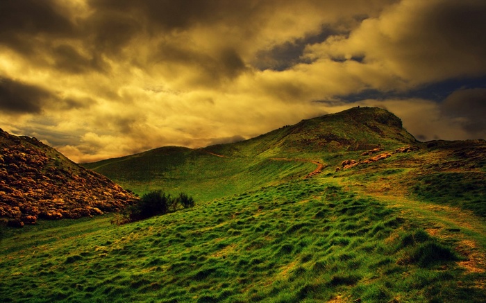 Green rolling hills under a dramatic cloudy sky