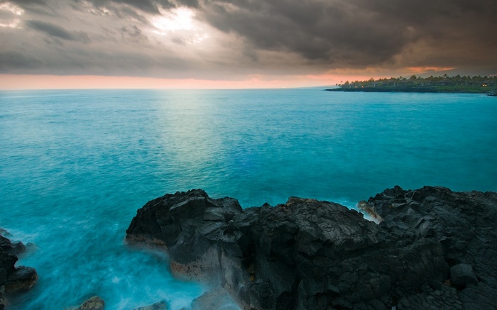 Ocean waves crash against dark rocks near a coastline
