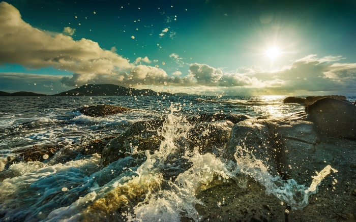 Waves crashing on rocky shore with sunlit sky