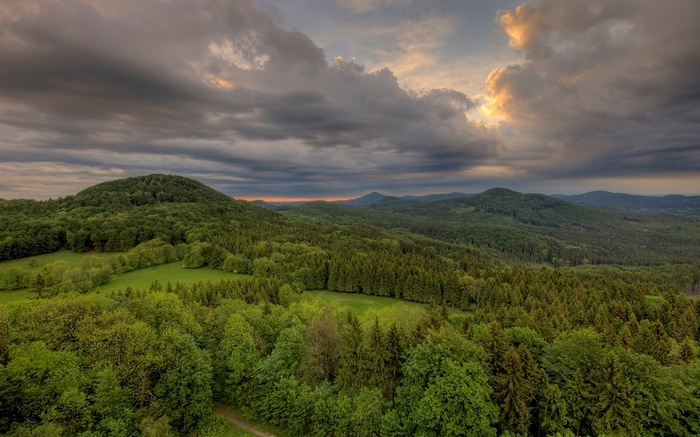 Overhead view of rolling green hills and forests under a cloudy sky