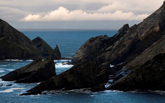 Jagged coastal cliffs meet the ocean under a cloudy sky.