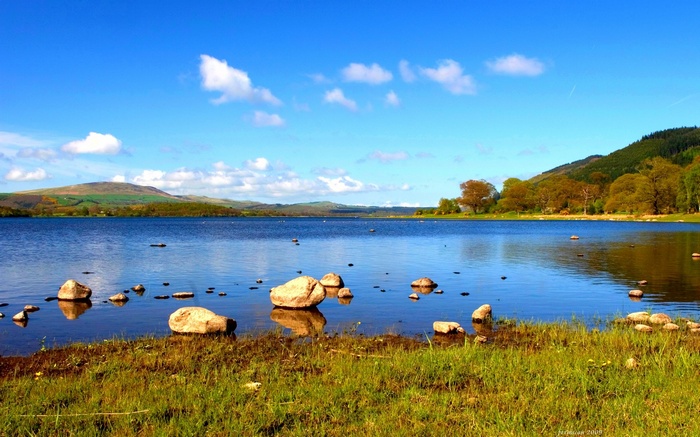 Lake with rocks and hills under a blue sky
