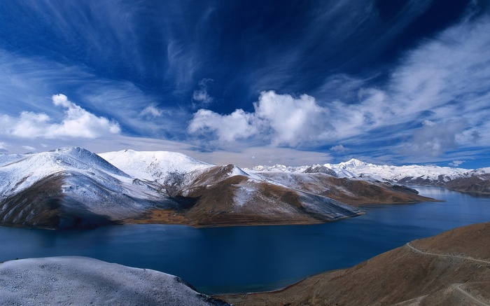 Snow-capped mountains surround a deep blue lake under a cloudy sky.
