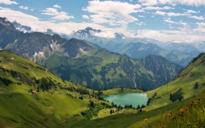 Alpine lake surrounded by green mountains and cloudy sky