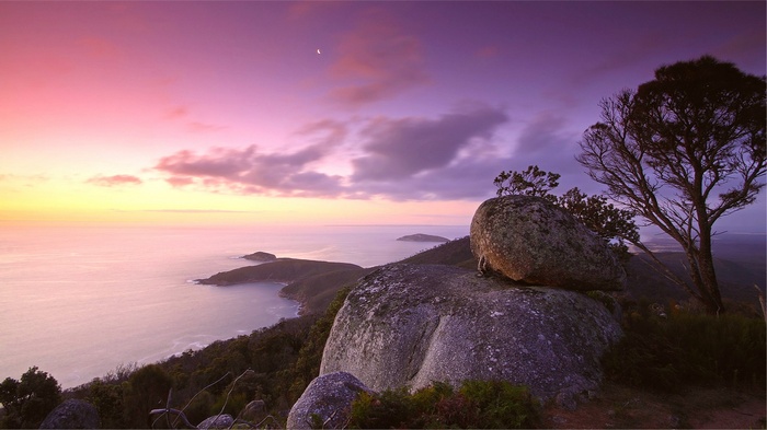Sunset over a rocky coastline with a crescent moon