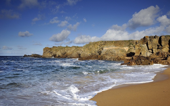 Waves crash on a sandy beach with rocky cliffs