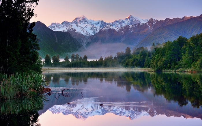 Snow-capped mountains reflected in a calm lake at sunrise