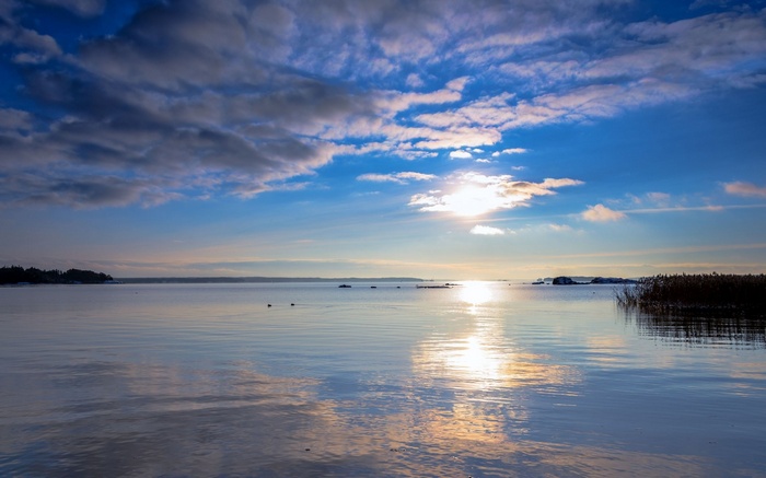 Calm lake at sunset with clouds and sun reflection