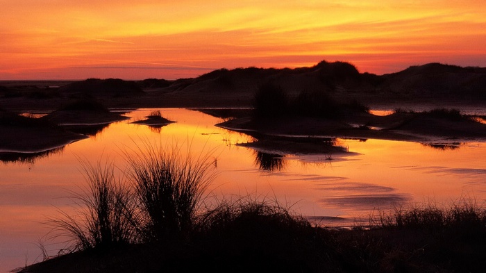 Sunset over water and sand dunes with grass