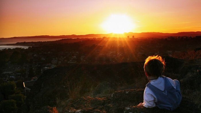Boy watching sunset over a city and ocean