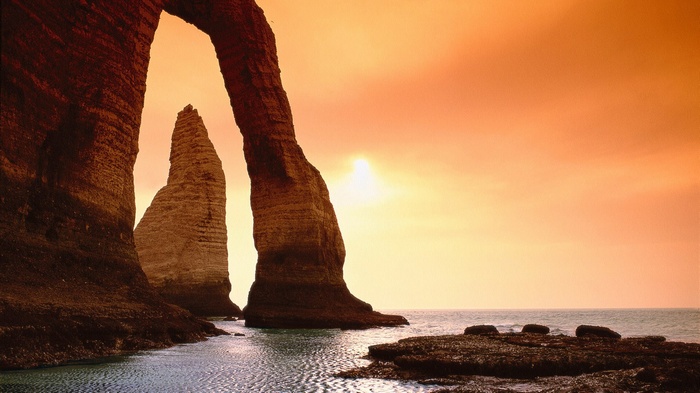 Arch rock formation over the sea at sunset