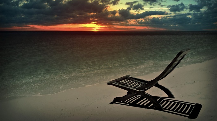 Empty lounge chair on a beach at sunset