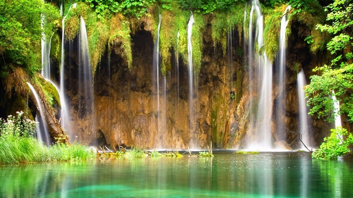 Waterfalls cascading over mossy rocks into a clear turquoise lake