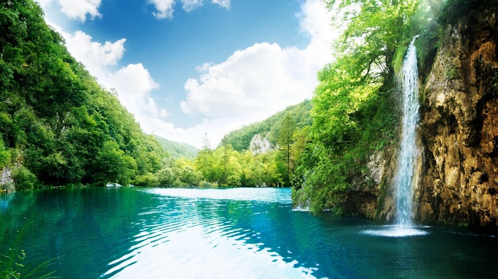 Waterfall cascading into a turquoise lake surrounded by green forest
