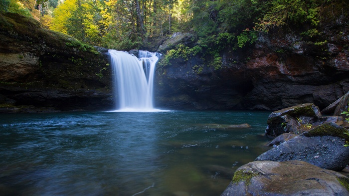 Waterfall cascading into a blue pool surrounded by rocks and trees