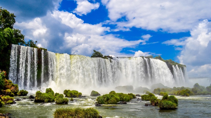 Wide waterfall with green rocks and blue sky