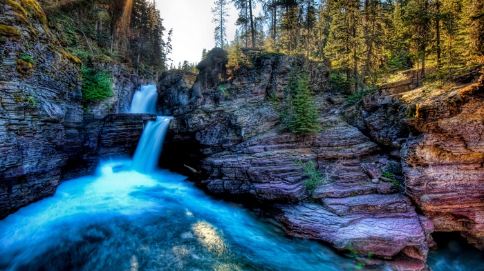 Waterfall cascading into a turquoise river in a rocky gorge