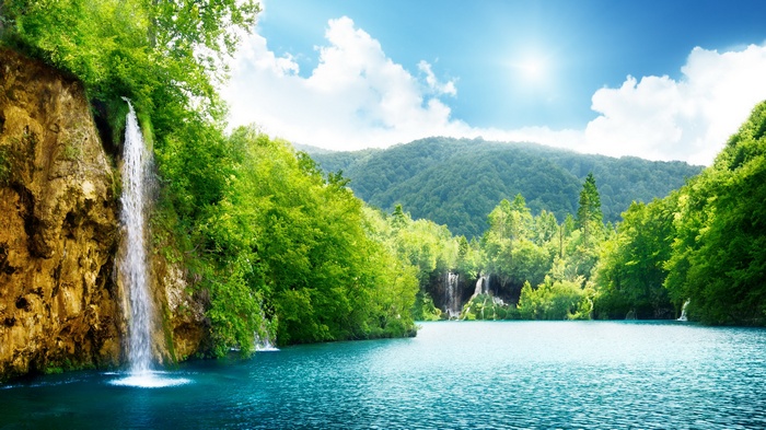 Waterfall cascading into a turquoise lake surrounded by green forest