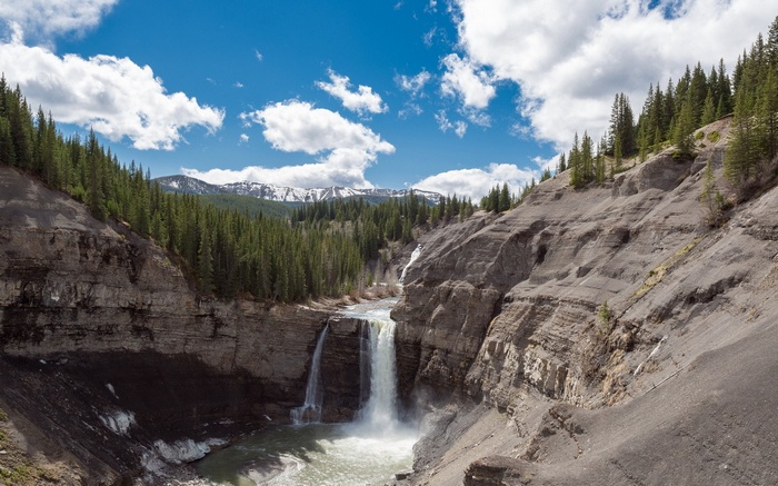 Waterfall in a rocky canyon with pine trees and mountains