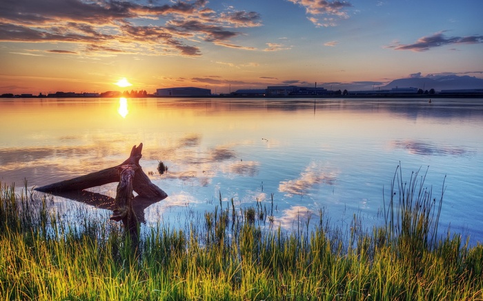 Sunset over a calm lake with industrial buildings