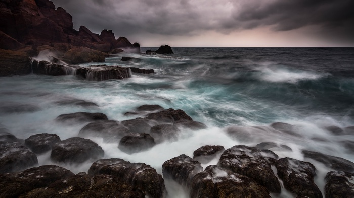 Waves crashing on rocky shore under stormy sky