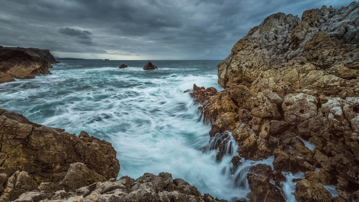 Waves crashing against rocky coastline under cloudy sky