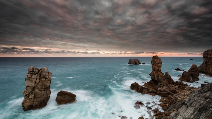 Rocky coast with waves crashing under cloudy sky
