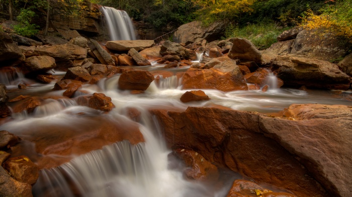Waterfall flowing over reddish-brown rocks in a forest