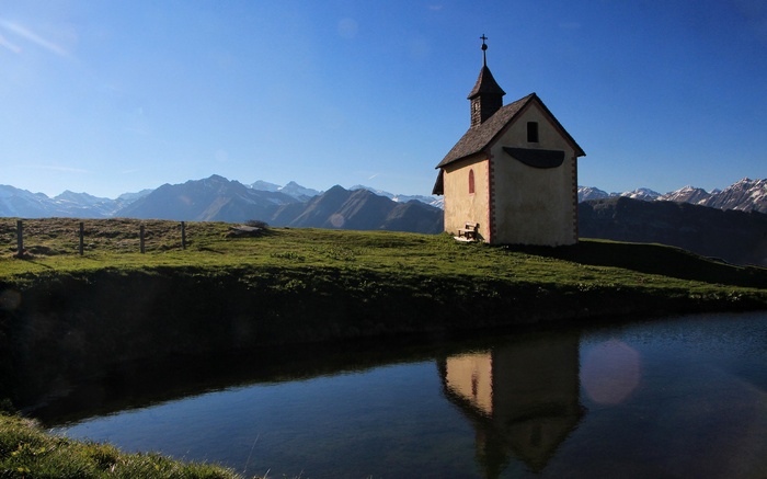 Chapel on a grassy hill overlooking mountains with a pond
