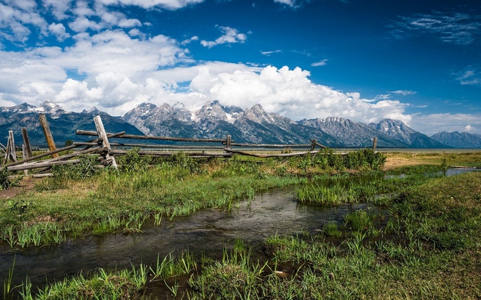 Wooden fence and stream with mountains in the background
