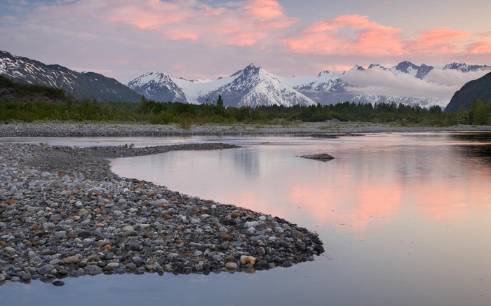Snow-capped mountains reflected in a river at sunset