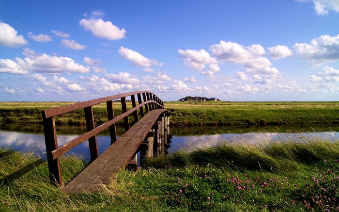 Wooden bridge over a canal with green fields and clouds
