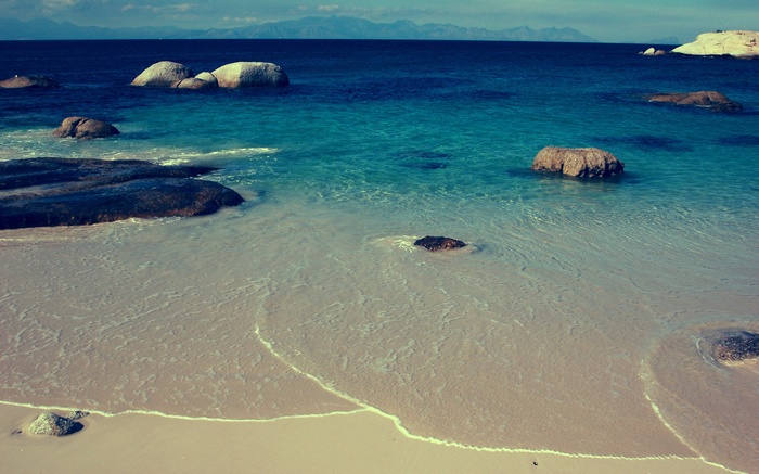 Rocky beach with clear blue water and distant mountains