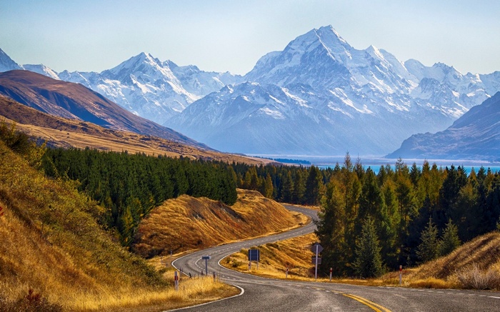 Winding road through autumn landscape towards snow-capped mountains