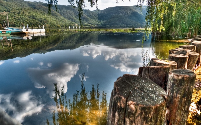 Lake with boats and reflections of mountains and clouds