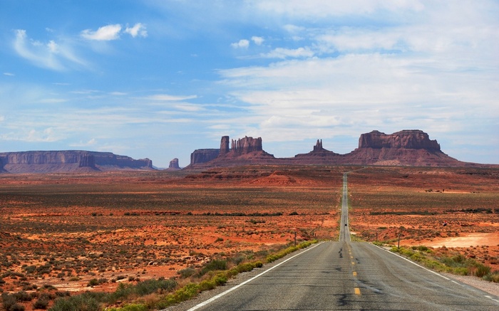 Monument Valley road with mesas under a blue sky