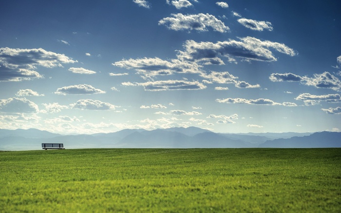 Bench on a grassy field with mountains and clouds