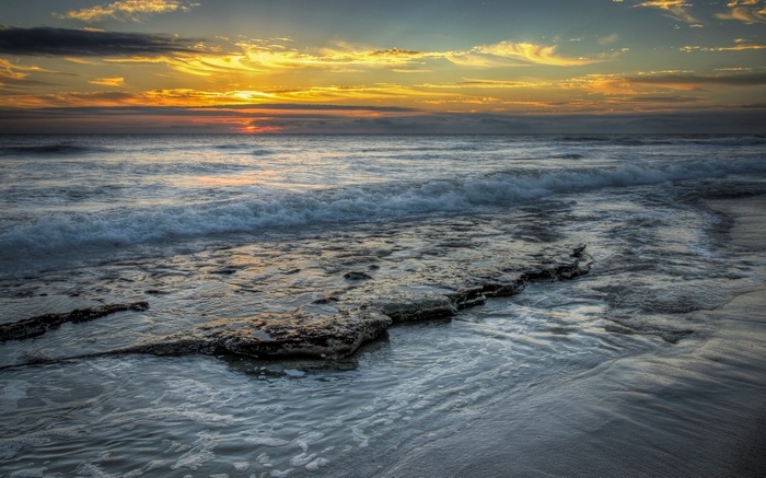 Sunset over the ocean with waves crashing on rocks