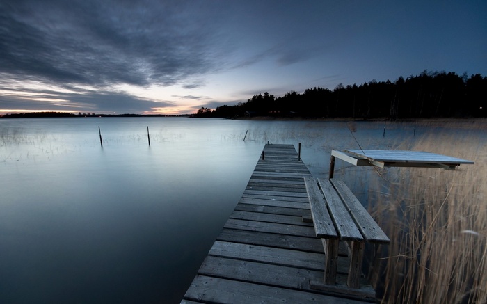 Wooden dock and bench on a calm lake at dusk