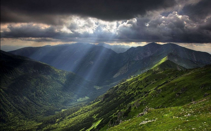 Sunbeams through clouds over a mountain valley
