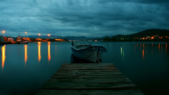 Boat docked at pier at dusk with city lights